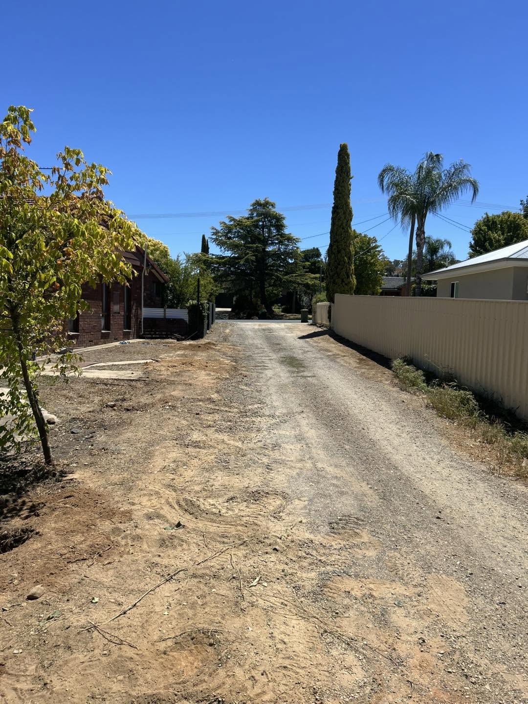 A cream Colorbond fence along a tree-lined driveway – a real job by Anesbury Fencing & Construction in Wagga Wagga