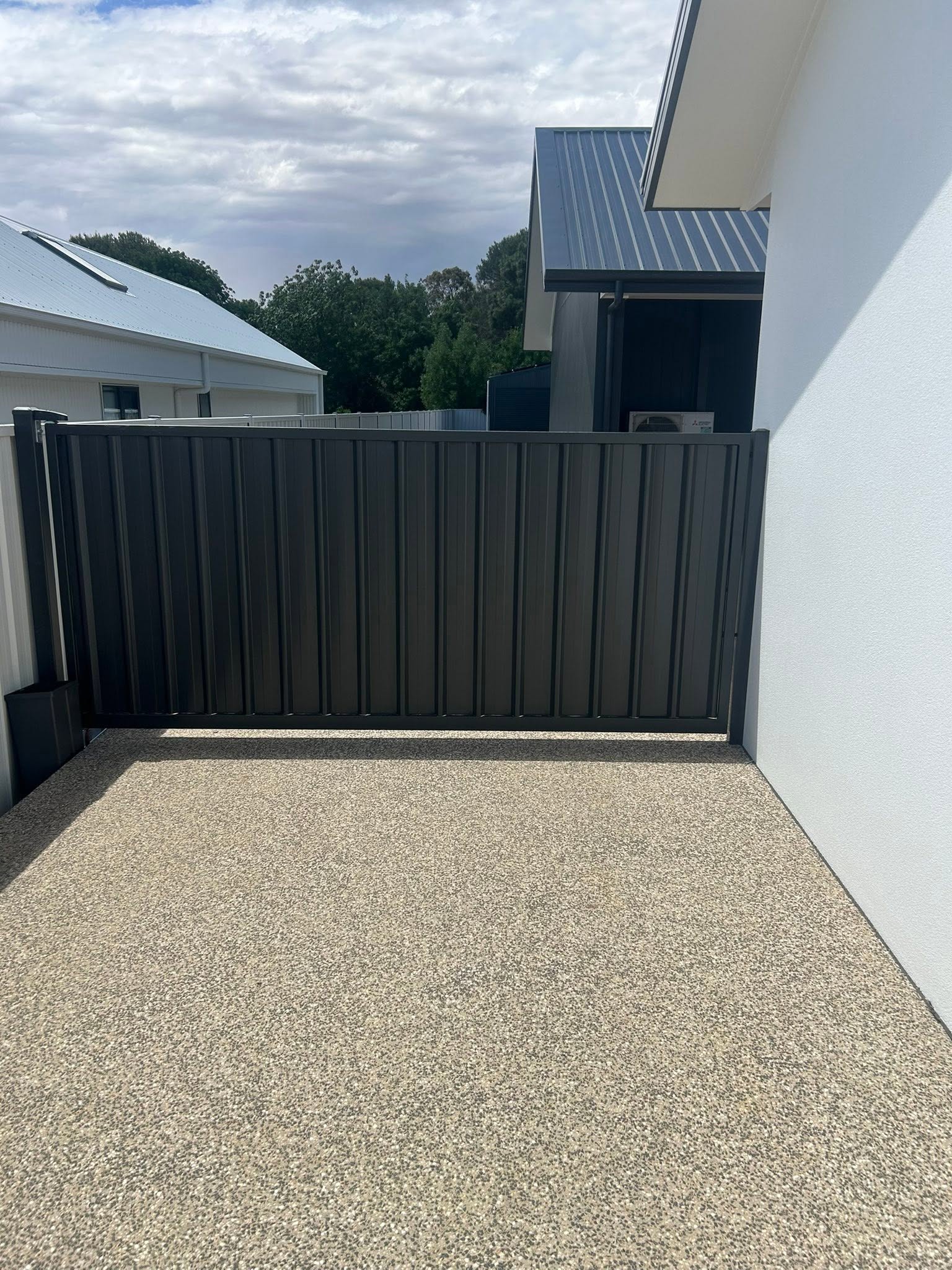 A dark grey Colorbond fence against a white wall – a real job by Anesbury Fencing & Construction in Wagga Wagga