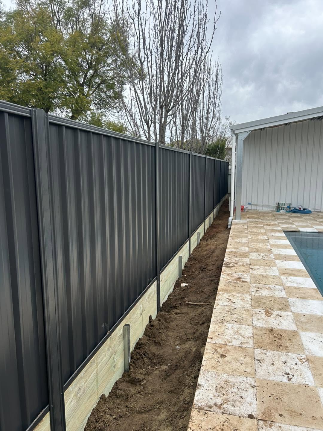A dark Colorbond fence and sleeper retaining by a pool area – a real job by Anesbury Fencing & Construction in Wagga Wagga