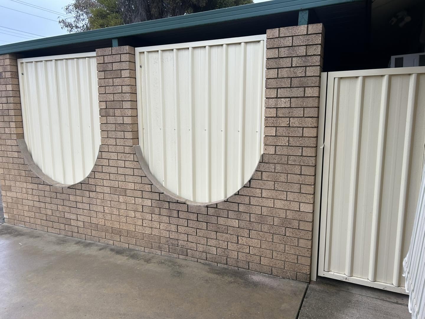 A cream Colorbond fence with arched infill panels against brick