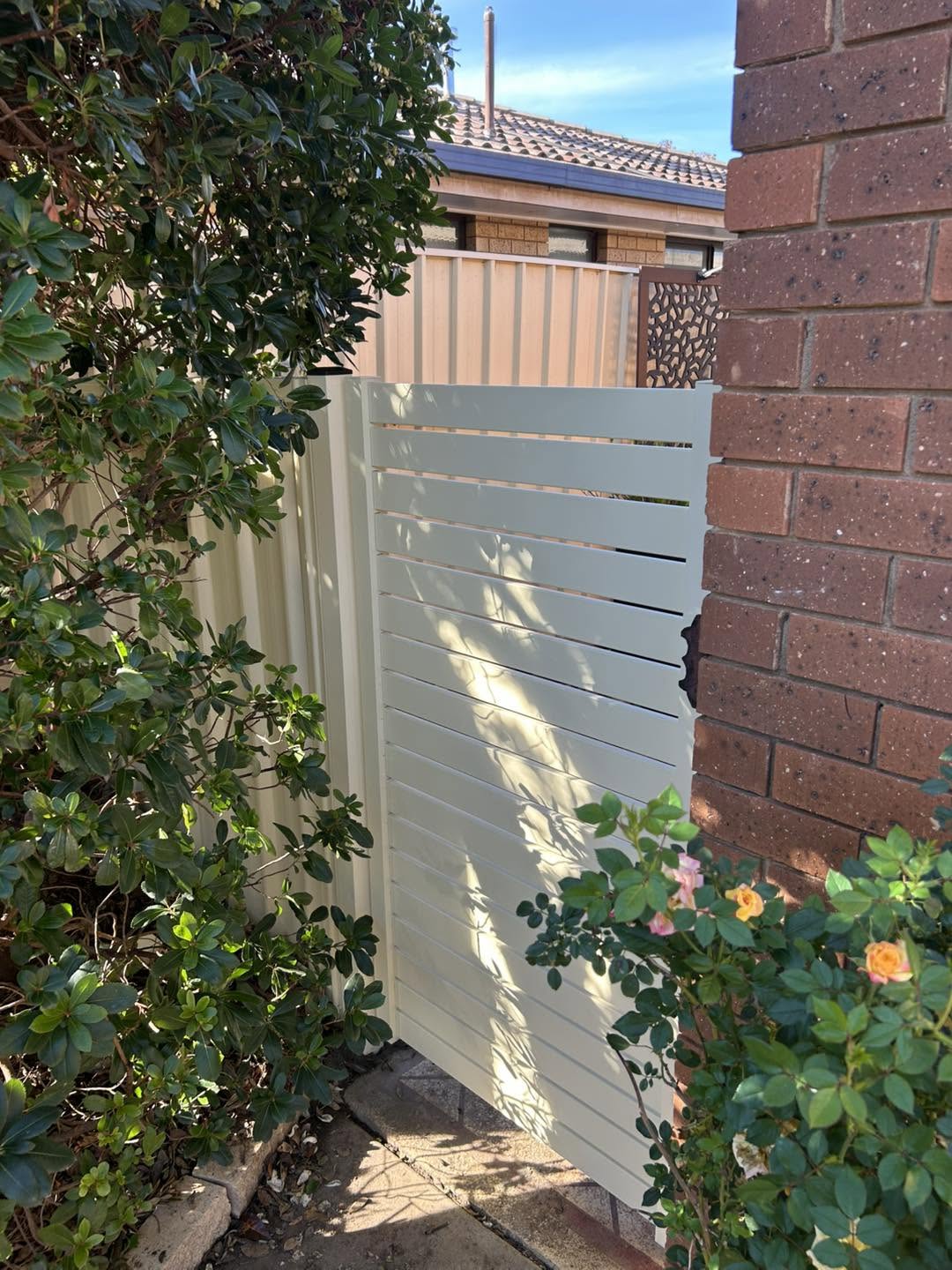 A white slat gate beside a brick home and roses